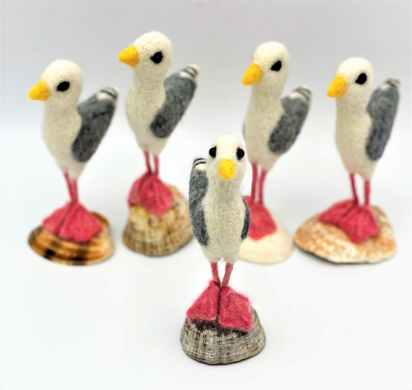 group of five needle felted seagulls standing on sea shells, white, black, grey wings, pink legs and feet