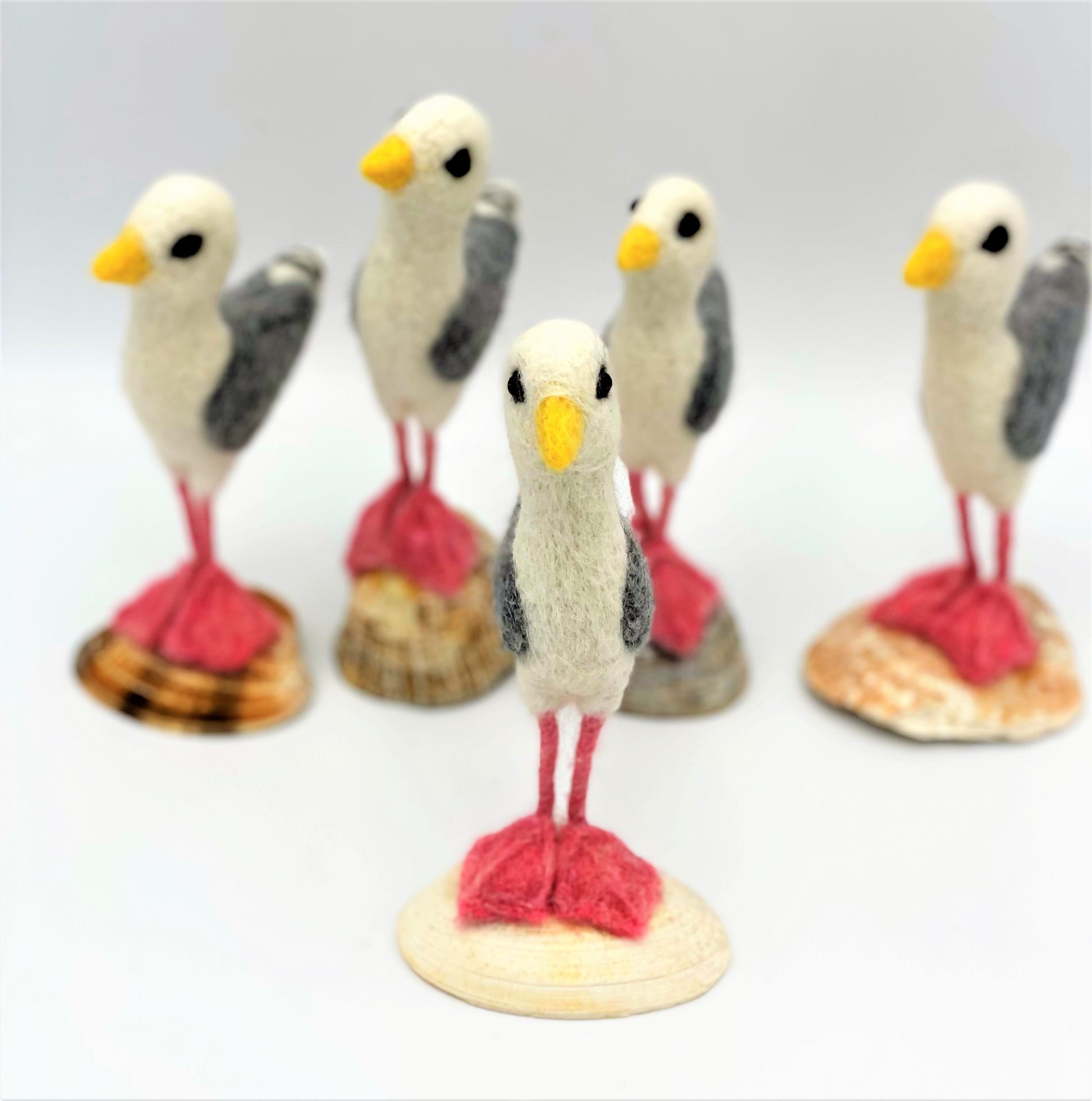 group of five needle felted seagulls standing on sea shells, white, black, grey wings, pink legs and feet