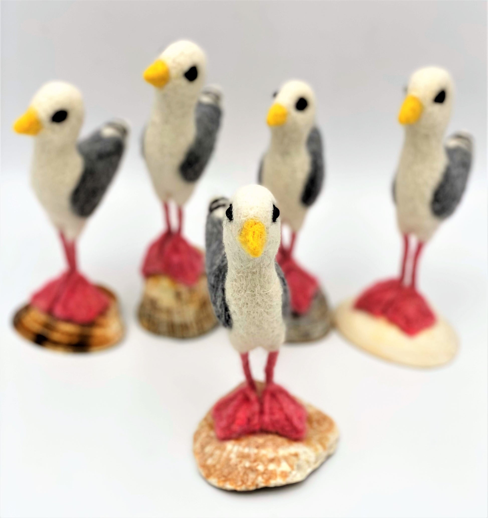 group of five needle felted seagulls standing on sea shells, white, black, grey wings, pink legs and feet