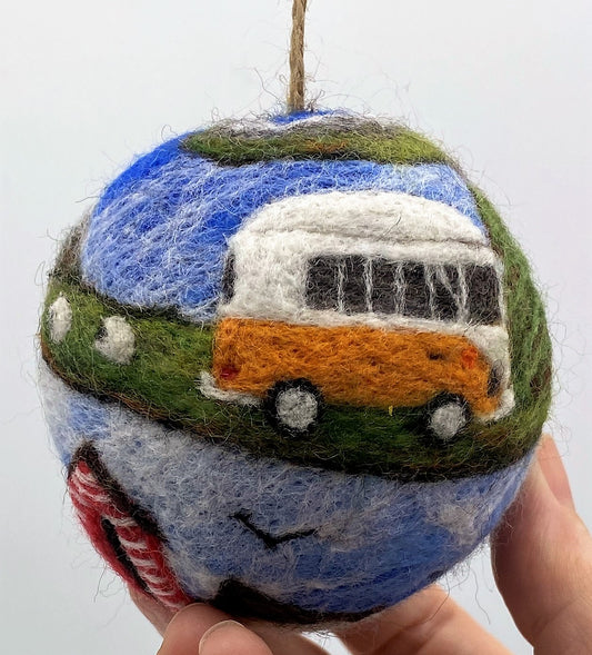 picture of a woollen bauble covered in a spiralling design depicting an orange  VW style van travelling through the mountains, past sheep, a camping site and concluding at a red striped beach hut by the sea